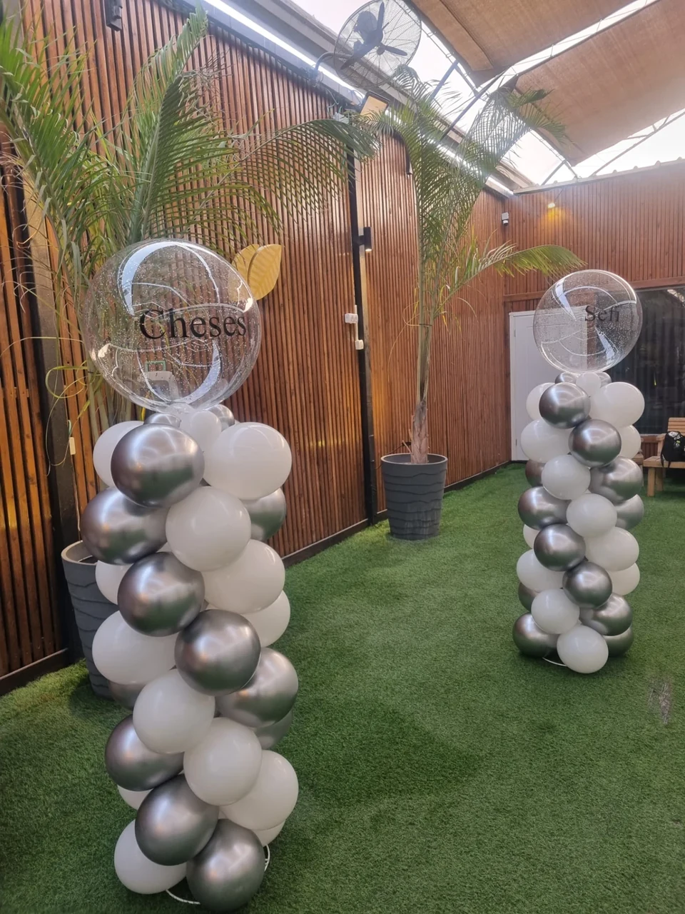 שני עמודי בלונים בלבן וכסף עם בלונים שקופים וכיתוב אישי