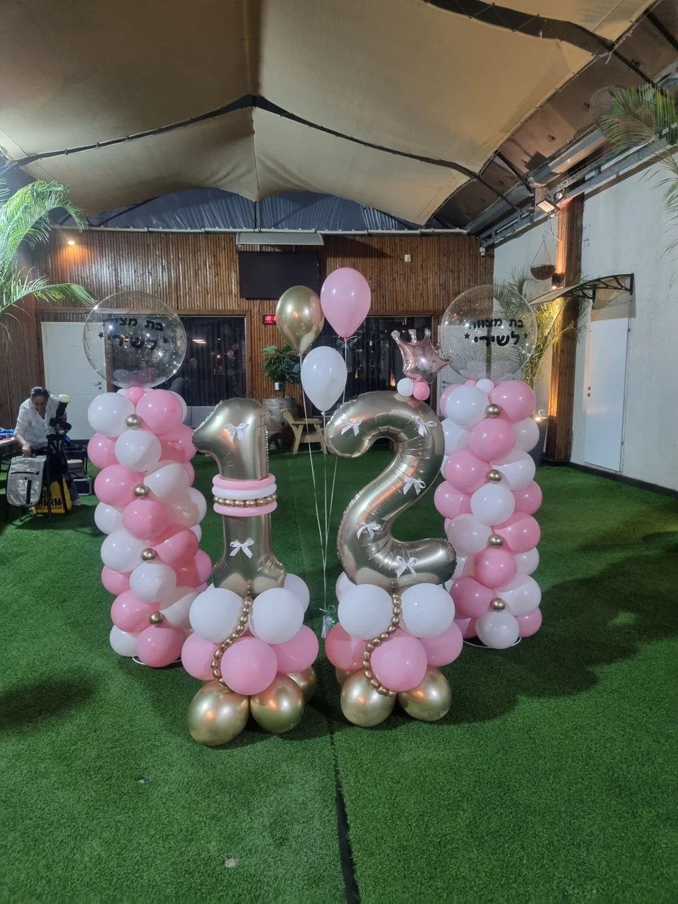 עיצוב יום הולדת 12 עם ספרות כסופות ושני עמודי בלונים ורודים ולבנים